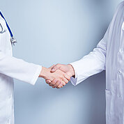 Deal! Concept of collaboration in medicine. Close up photo of two doctors' handshake on gray background