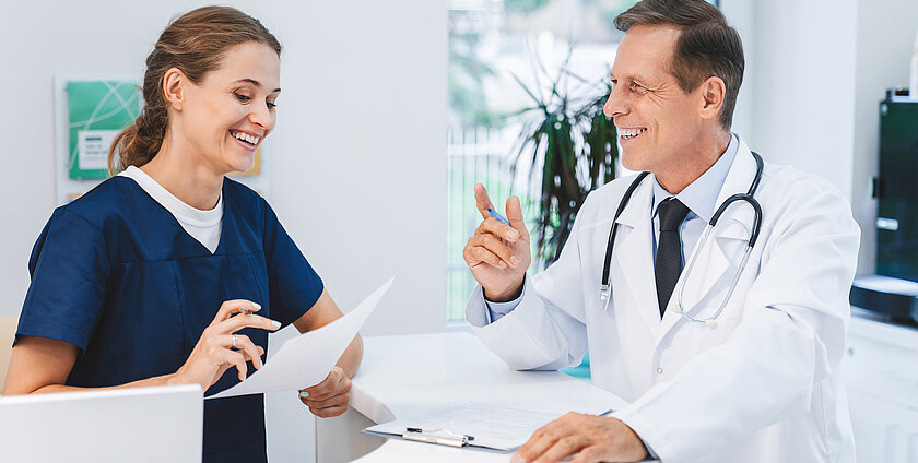 Senior doctor talking with nurse receptionist at hospital reception