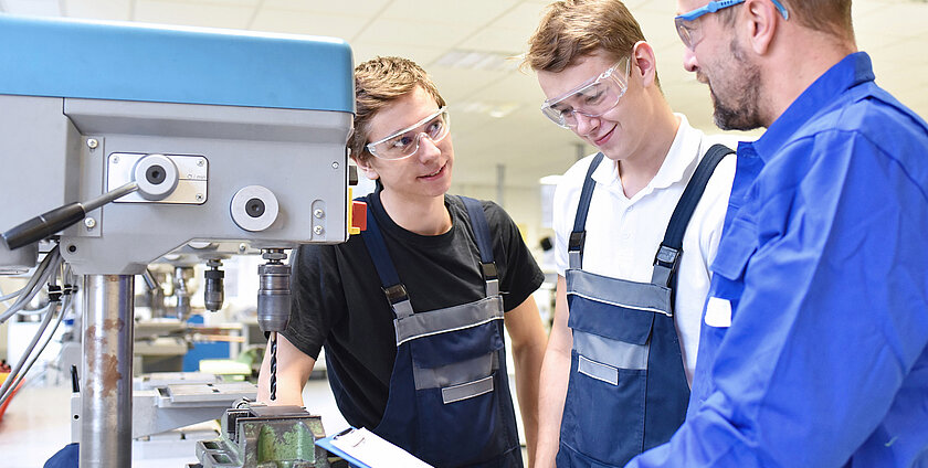 trainer and apprentice in technical vocational training at a drilling machine